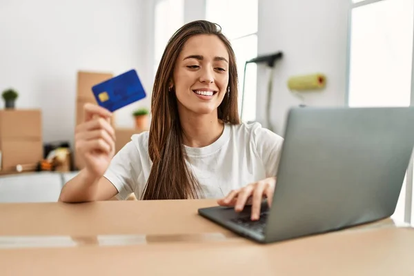 年轻的惊慌失措的女人带着自信的笑容在新家使用信用卡和笔记本电脑 — 图库照片