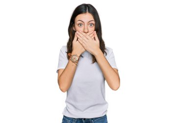 Gündelik beyaz tişört giyen genç ve güzel bir kadın yanlışlıkla elleriyle ağzını kapatırken şok oldu. gizli kavram. 