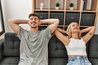 Kafkasyalı genç çift ellerini başının üstüne koyup evdeki kanepede oturuyorlar..