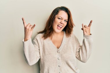 Kafkasyalı genç bir kadın gündelik kıyafetler giyip çılgın bir ifadeyle bağırıyor ve elleri havada rock sembolü yapıyor. Müzik yıldızı. ağır müzik konsepti. 