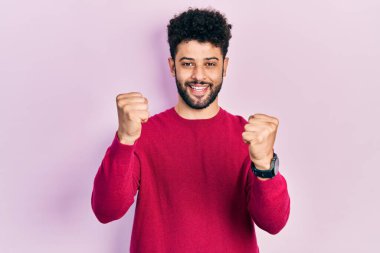 Sakallı, sıradan pembe kazaklı genç Arap adam gururla bağırıyor, zaferi kutluyor ve başarıyı kollarını kaldırarak kutluyor. 