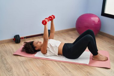 Genç Afrikalı Amerikalı kadın spor merkezinde dambıl kullanıyor.