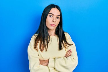 Genç esmer kadın sıradan bir kazak giyiyor şüpheci ve gergin, yüzünde çapraz kollu tasvip etmeyen bir ifade var. negatif kişi. 