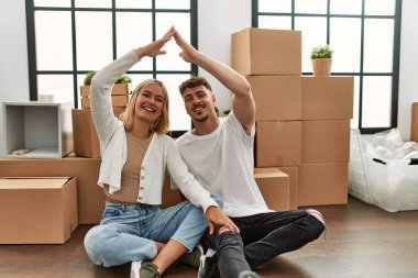 Genç beyaz çift gülümseyerek yeni evlerinde ev sembolü yapıyor..