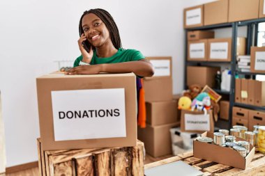 Gönüllü üniforma giyen genç Afro-Amerikan kadın yardım merkezindeki akıllı telefondan konuşuyor.