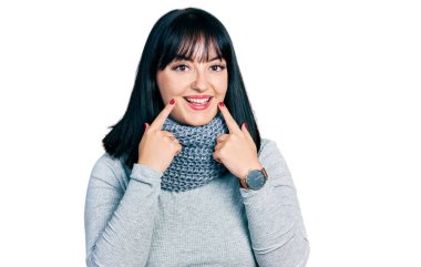 Genç İspanyol asıllı, kışın atkı takan, ağzı açık gülümseyen, parmakları işaret eden ve neşeli gülümsemeye zorlayan bir kadın. 