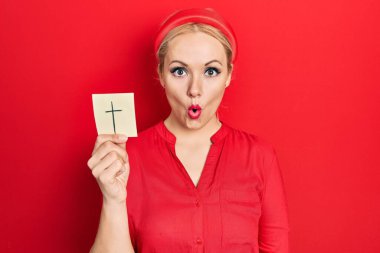 Sarışın genç bir kadın Katolik haçı tutuyor. Korkmuş ve şaşırmış bir şekilde ağzı açık, inançsız bir yüz. 