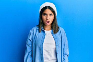 Şok suratlı, sevimli yün şapkalı genç Latin kadın şüpheci ve alaycı görünüyor, ağzı açık kalınca şaşırıyor. 