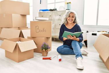 Orta yaşlı, kır saçlı, gülümseyen, yeni evinde mutlu bir kitap okuyan kadın..