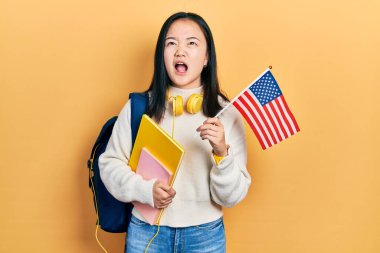 Genç Çinli değişim öğrencisi elinde Amerika bayrağı tutarken kızgın ve öfkeli çığlıklar atıyor öfkeyle bağırıyor, öfkeyle yukarı bakıyor.. 