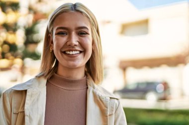 Genç sarışın kız gülümsüyor, mutlu bir şekilde şehirde duruyor..