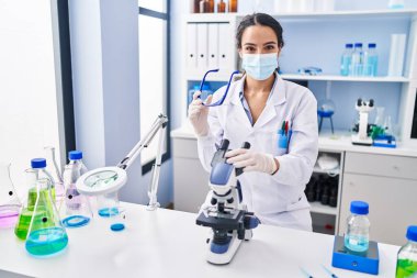 Laboratuvarda mikroskop kullanan genç İspanyol kadın bilim adamı üniforması giyiyor.