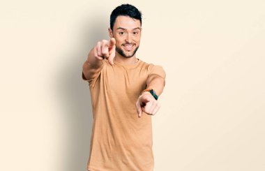 Sakallı, sıradan tişörtlü İspanyol bir adam seni ve kamerayı parmaklarıyla gösteriyor, gülümsüyor ve neşeli. 