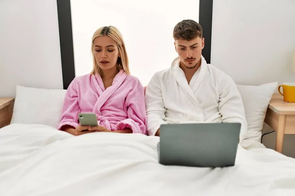 Laptop Akıllı Telefon Kullanan Beyaz Bir Çift Evdeki Yatakta Oturuyor — Stok fotoğraf
