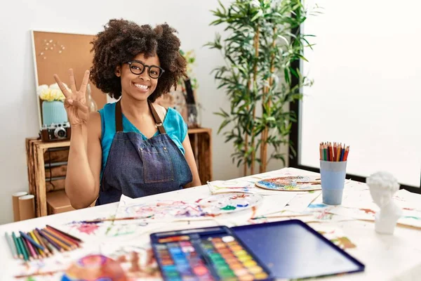 美丽的非洲裔美国女人 在艺术工作室里画着非洲的头发 带着自信和快乐的笑容 用手指指指着第三号 — 图库照片