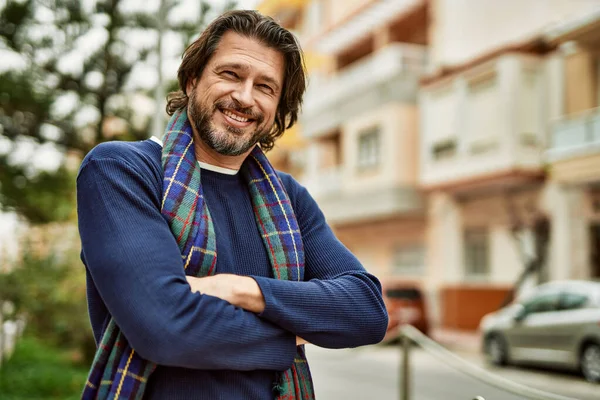 Kasabada kollarını kavuşturup gülümseyen orta yaşlı yakışıklı bir adam.