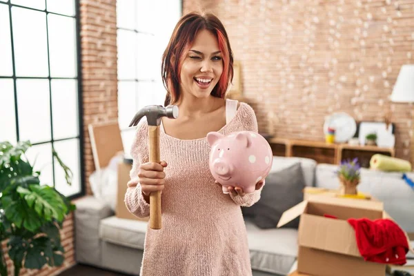 年轻的高加索女人抱着小猪银行在新的家眨眼看着相机 带着性感的表情 开心而快乐的脸 — 图库照片