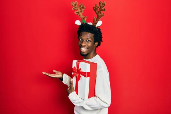 Mladý Africký Američan Nosí Jelení Vánoční Klobouk Drží Dárek Ukazuje — Stock fotografie