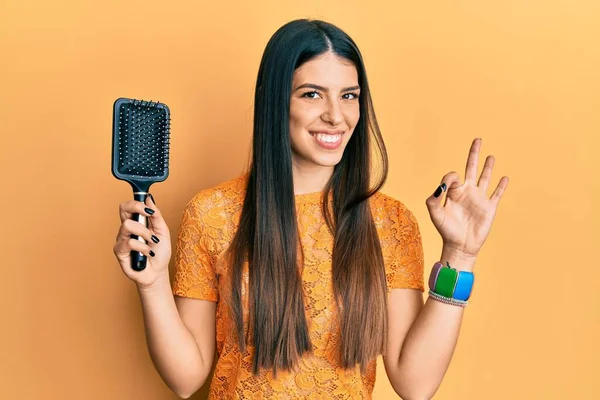 Young Hispanic Woman Holding Hairbrush Doing Sign Fingers Smiling Friendly — ストック写真