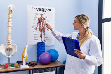 Fizyoterapi kliniğindeki anatomi raporunu gösteren fizyoterpist üniforma giyen genç sarışın kadın.