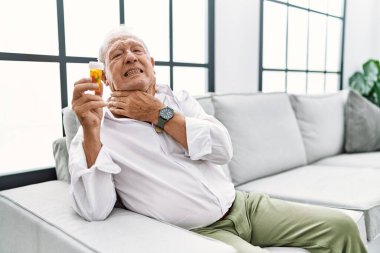 Yaşlı adam elinde haplar, boynuna dokunuyor, boğazında grip, mantar ve enfeksiyon var. 