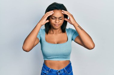 Genç Afrikalı Amerikalı kız gündelik kıyafetler giyiyor. Baş ağrısı çekiyor. Acı ve migren yüzünden çaresiz ve stresli. Eller başının üstünde.. 