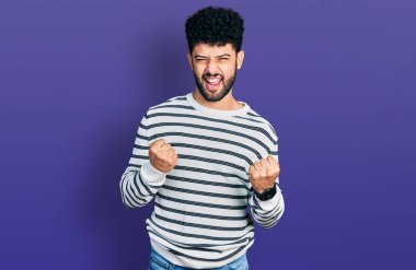 Sakallı, sıradan çizgili süveter giyen genç Arap adam kolları havada ve gözleri kapalı bir şekilde başarıyı kutluyor ve şaşırıyor. Kazanan konsept. 