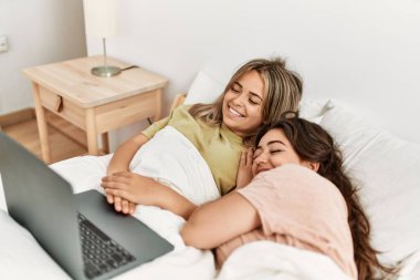 Genç çift yatak odasında dizüstü bilgisayar kullanarak film izliyor.