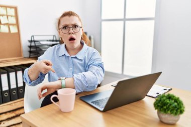 Ofiste çalışan genç kızıl saçlı kadın bilgisayarını kullanıyor. Aceleyle saati, sabırsızlığı ve gecikmeyi işaret ediyor. 