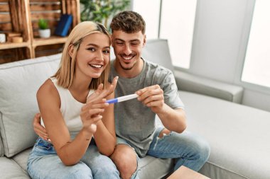 Genç beyaz çift mutlu bir şekilde gülümsüyor. Evde hamilelik testi yapıyorlar..