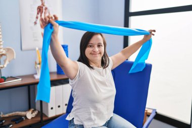 Down sendromlu kadın fizik tedavi kliniğinde elastik bant kullanarak rehabilitasyon seansı yapıyor.