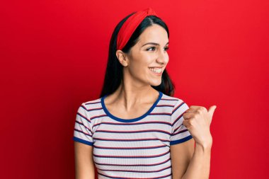 Gündelik kıyafetler giyen, gülen yüzlü genç İspanyol kadın başparmağıyla yan tarafa bakıyor ve işaret ediyor.. 