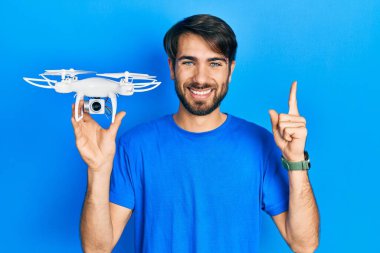 İHA 'yı elinde tutan genç İspanyol bir adam bir fikir veya soruyla gülümsüyor ve mutlu bir yüzle işaret ediyor. 
