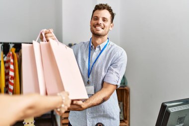 Genç İspanyol esnaf gülümseyerek giyim mağazasındaki müşterilere alışveriş torbaları veriyor..