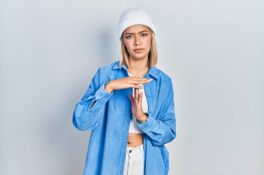 Yün şapka takan güzel sarışın kadın. Elleriyle jest yapıyor, hayal kırıklığına uğramış ve ciddi bir yüz ifadesi takınıyor. 