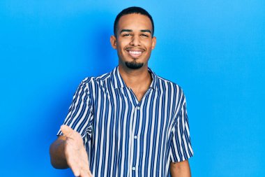 Genç Afro-Amerikan adam günlük kıyafetler giyip gülümseyerek dostça el sıkışarak selamlama ve hoş geldin diyor. başarılı iş. 