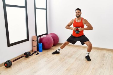Genç Arap adam gülümsüyor spor merkezinde kettlebell ile antrenman yapıyor.