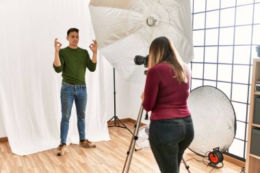 Young man at photography studio relax and smiling with eyes closed doing meditation gesture with fingers. yoga concept. 