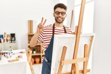 Sanat stüdyosundaki Arap genç adam kameraya bakıp zafer işareti yapıyor. İki numara.. 