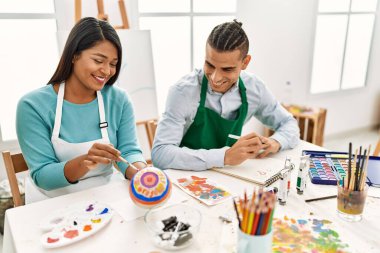 Genç Latin ressam çift gülümseyen mutlu tablo sanat stüdyosunda masada oturuyor.