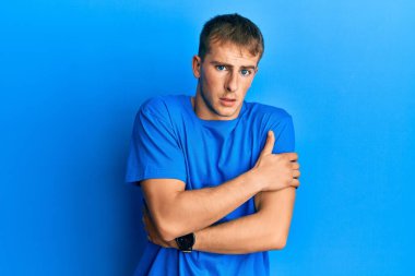 Kafkasyalı genç bir adam günlük mavi tişört giyiyor. Kış soğuğu için titriyor ve donuyor. Yüzünde üzgün ve şok ifadesi var. 