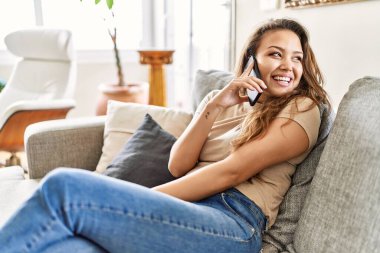 Genç İspanyol kız akıllı telefonda konuşuyor. Evdeki kanepede oturuyor..