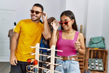 Genç Latin çift gülümseyerek mağazadan güneş gözlüğü seçiyor..