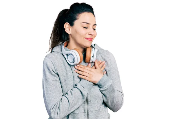 若いヒスパニック系の女性は ジムの服を着て 胸に手で笑みを浮かべてヘッドフォンを使用して 目の顔に感謝のジェスチャーで閉じます 健康の概念 — ストック写真