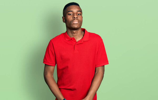 Young african american man wearing casual red t shirt looking sleepy and tired, exhausted for fatigue and hangover, lazy eyes in the morning.