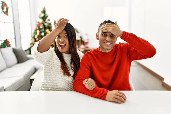 Young Latin Couple Sitting Table Christmas Tree Surprised Hand Head — Stockfoto