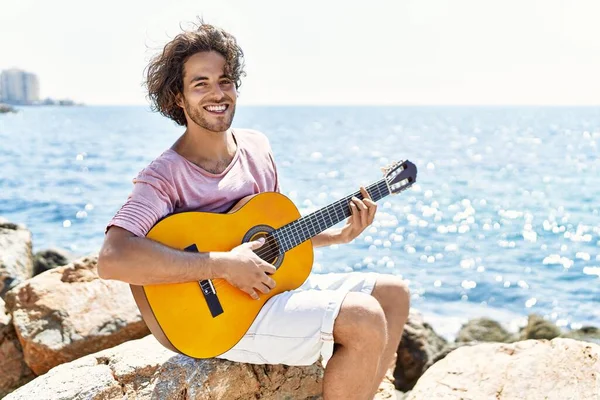 Genç İspanyol adam klasik gitar çalıyor plajda rock 'ın üzerinde oturuyor..