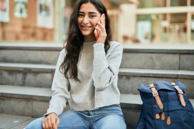 Genç ortadoğulu kız gülümsüyor. Şehirdeki akıllı telefondan konuşuyor..