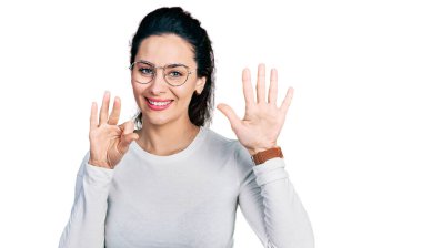 Genç İspanyol kadın gündelik kıyafetler giyer ve sekiz numaralı parmaklarıyla gülümseyerek mutlu ve kendinden emin bir şekilde işaret eder.. 