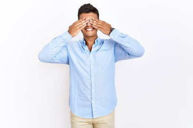 Genç İspanyol gömlekli adam izole edilmiş arka planda dikiliyor. Gözleri neşeli ve komik bir şekilde gülümsüyor. kör kavram. 